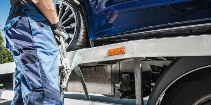 A tow truck driver fastening a blue vehicle to the bed of a flat bed tow truck