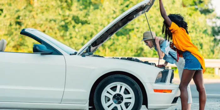 Two women broken down on the side of the road with the hood up and they are looking at it bewildered