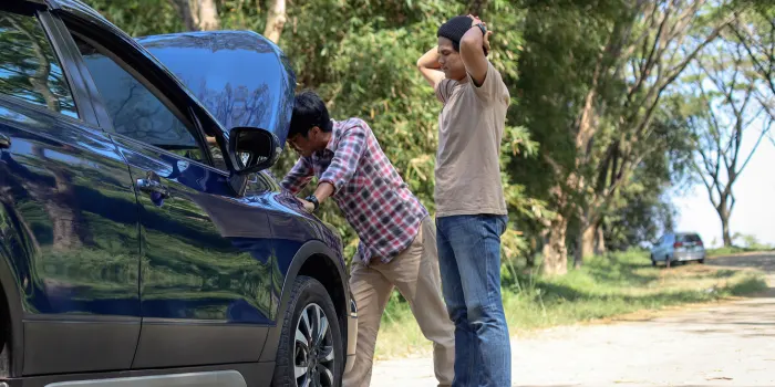 A couple of fellas on the side the road with their car broke down and the hood up with them starring at it in disbelief