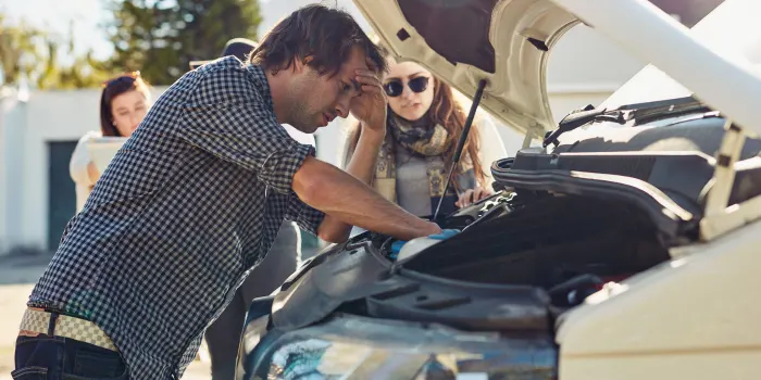 A man who needs a tow, looking under his hood, frustrated